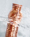 Eine gehämmert aussehende Kupferwasserflasche, die mit klarem Wasser bespritzt wird.