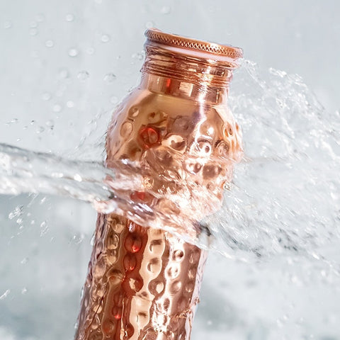 Eine gehämmert aussehende Kupferwasserflasche, die mit klarem Wasser bespritzt wird.