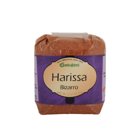 Ein Klarsichtbeutel mit rötlich-braunem Gewürzpulver der Marke Gwürzhüsli, beschriftet mit „Harissa Bizarro“ auf einem violett-cremefarbenen Etikett.