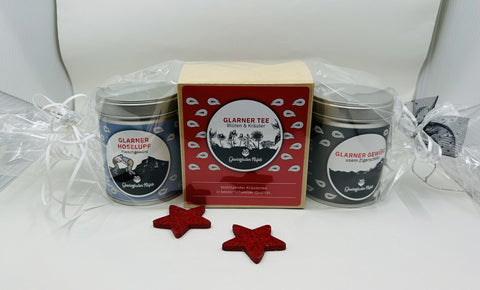 Ein Geschenkset mit zwei Gewürzdosen und einer Teeschachtel „Glarner“, in Folie verpackt mit zwei roten Glitzersternen.