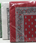 Eine Reihe von fünf Packungen Papierservietten in verschiedenen Farben (Lila, Schwarz, Grün, Weiß und Rot), jeweils mit einer traditionellen Paisley-Muster-Bordüre und kleinen Tropfenmotiven.