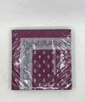 Eine eingeschweißte Packung lila Papierservietten mit einer schwarz-weißen Paisley-Bordüre und passendem Tropfenmuster in der Mitte.
