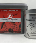 Zwei Behälter mit Knoblauch granuliert von Landolt Hauser AG: ein großer grauer Kunststoffkübel mit rotem Etikett und eine kleinere silberne Gewürzdose mit einem Segelschiff-Logo.