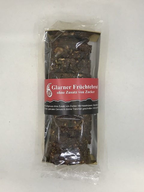 Draufsicht auf ein Glarner Früchtebrot in Klarsichtverpackung; das geschnittene dunkle Brot ist mit ganzen Nüssen gefüllt und trägt eine rote Banderole mit der Aufschrift „ohne Zusatz von Zucker“.