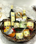 Ein dunkler Weiden-Geschenkkorb, verpackt in Klarsichtfolie und mit Schleifen verziert, gefüllt mit Flaschen Terra Verde Essig und Olivenöl, Gläsern mit Soßen und Oliven, einer Packung Pasta und MySpice Gewürzdosen.