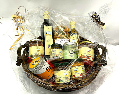 Ein dunkler Weiden-Geschenkkorb, verpackt in Klarsichtfolie und mit Schleifen verziert, gefüllt mit Flaschen Terra Verde Essig und Olivenöl, Gläsern mit Soßen und Oliven, einer Packung Pasta und MySpice Gewürzdosen.