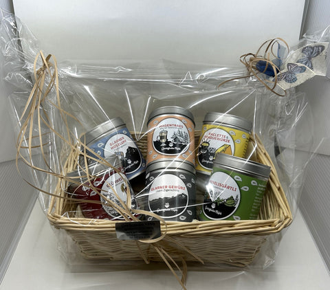 Ein heller Weidenkorb mit fünf bunten Gewürzdosen, in Zellophan verpackt und mit einem Schmetterling verziert.