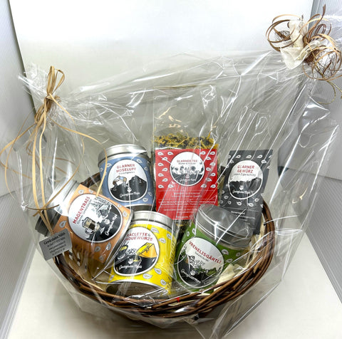 Ein Geschenkkorb mit Schweizer Gewürzdosen und Tees, verpackt in Klarsichtfolie und mit einer Schleife gebunden.