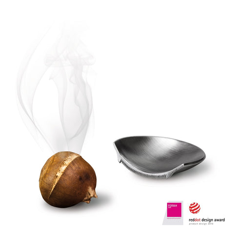 Eine geröstete, dampfende Kastanie neben einem kleinen Kastanienöffner aus Metall mit Designpreisen.