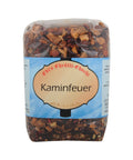 Eine Klarsichtpackung Früchtetee „Kaminfeuer“ von Edis Chrütli-Chuchi mit einer losen Mischung aus getrockneten Apfelstücken, Hibiskus und Hagebutte sowie einem hellblauen Etikett.