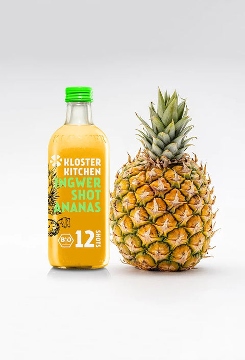Eine große Flasche Ananas-Ingwer-Shot steht neben einer ganzen Ananas.