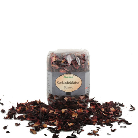 Ein Klarsichtbeutel mit getrockneten Karkadeblüten (Hibiskus) der Marke Gwürzhüsli, beschriftet mit „Karkadeblüten Bizarro“, wobei ein Teil der dunkelroten Blütenblätter davor auf der weißen Fläche verstreut liegt.