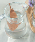 Kupferfeder-Infuser in einem Glaskrug mit Wasser neben zwei Trinkgläsern.