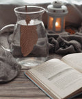 Gemütliche Szene mit einem Glaskrug, der einen Kupferfeder-Infuser enthält, einem offenen Buch und einer leuchtenden Laterne.