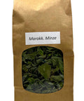 Eine braune Papiertüte mit einem kleinen Sichtfenster, das getrocknete grüne marokkanische Minzblätter zeigt, beschriftet mit einem weißen Etikett „Marokk. Minze“.
