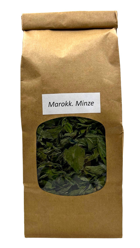 Eine braune Papiertüte mit einem kleinen Sichtfenster, das getrocknete grüne marokkanische Minzblätter zeigt, beschriftet mit einem weißen Etikett „Marokk. Minze“.