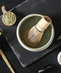 Gewurzladen Nafels Aufnahme von oben: Matcha-Besen in einer Schale mit Pulver und Zubehör auf einer Schieferunterlage.