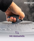 Nahaufnahme einer Hand, die den mixcover Thermo-Griff auf dem dampfenden, beschlagenen Deckel eines Küchengeräts hält. Text: „Mit Ablösehilfe“.