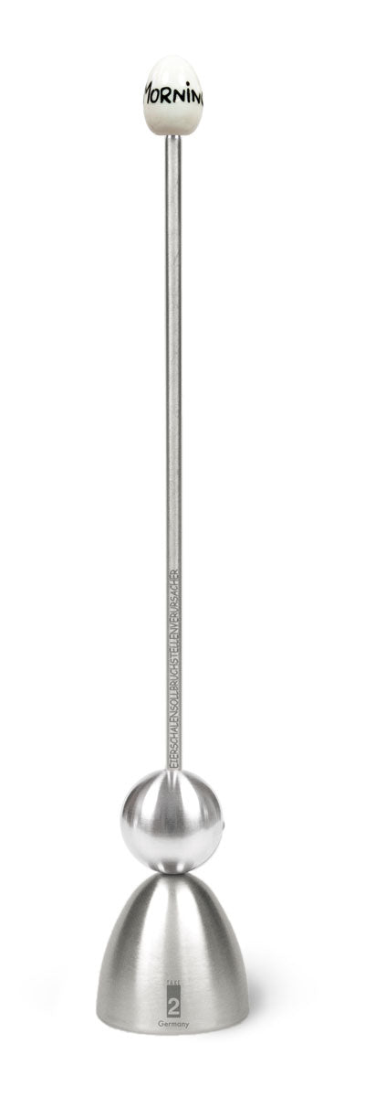 Ein Edelstahl-Eierschalensollbruchstellenverursacher „Clack“ von Take2 Germany mit langer Führungsstange, glockenförmigem Unterteil und einem weißen Keramikkopf mit der Aufschrift „MORNING“.