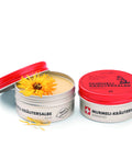 Zwei silberne 100-ml-Dosen der wärmenden „puralpina Murmeli-Kräutersalbe“, eine geschlossen und eine geöffnet, mit der glatten Salbe und einer leuchtend gelben Arnikablüte darauf.