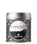Silberne Gewürzdose für "Glarner Gewürz usem Zigerschlitz" mit einem dunkelgrauen Etikett, das eine Berglandschaft und ein Paisleymuster zeigt, isoliert auf weißem Hintergrund.