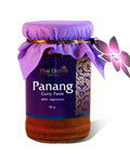 Ein Glas Thai Orchid Selection Panang Curry Paste (114g), als 100 % vegetarisch gekennzeichnet, mit einem lila Etikett, einer Stoffkappe und einem Schmetterlingsanhänger.