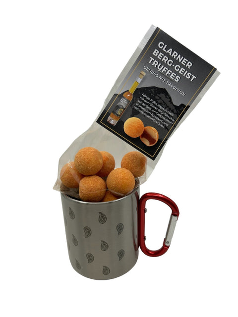 Ein durchsichtiger Beutel mit orange bestäubten „Glarner Berg-Geist Truffes“ in einem Edelstahlbecher mit rotem Karabinergriff und Paisley-Muster.