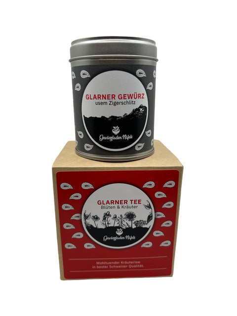 Eine dunkle Gewürzdose auf einer würfelförmigen Box mit Glarner Tee und Kräutern.