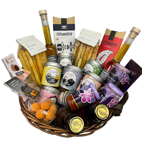 German: Ein großer Weidenkorb gefüllt mit verschiedenen Schweizer Gourmet-Lebensmitteln und verpackten Waren.