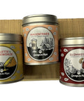 Drei etikettierte Gewürzdosen für Raclette, Glühwein und eine spezielle Mischung, präsentiert auf einem Holzpodest.