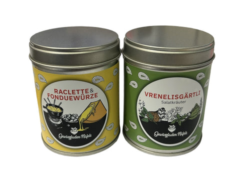 Zwei Gewürzdosen stehen nebeneinander: links eine gelbe Dose "Raclette & Fonduewürze" und rechts eine grüne Dose "Vrenelisgärtli Salzkräuter".