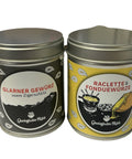 Zwei Gewürzdosen stehen nebeneinander: links eine schwarze Dose "Glarner Gewürz usem Zigerschlitz" und rechts eine gelbe Dose "Raclette & Fonduewürze".