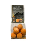 Ein stehender, transparenter Zellophanbeutel gefüllt mit orange bestäubten „Glarner Berg-Geist Truffes“, oben versehen mit einem schwarz-grauen Etikett, das eine Abbildung der Trüffel und einer Likörflasche zeigt.