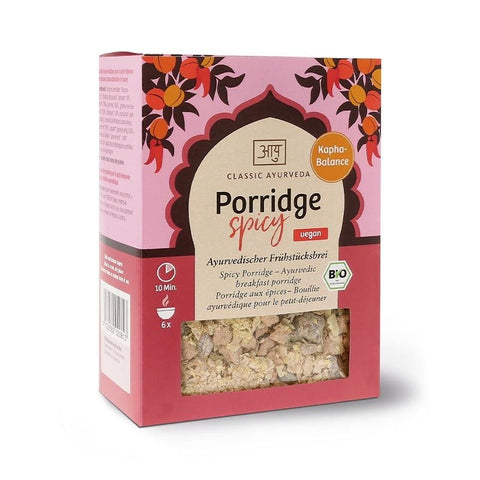 Eine Packung „Porridge Spicy“ von Classic Ayurveda, gekennzeichnet als vegan und Bio-zertifiziert, mit einem dekorativen rosa-orangen Design und einem Sichtfenster, das die trockene Hafer-Gewürz-Mischung zeigt