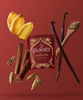 Pukka Vanilla Chai Teebeutel umgeben von Ingwer, Vanilleschoten, Zimt und Kardamom-Gewürzen.