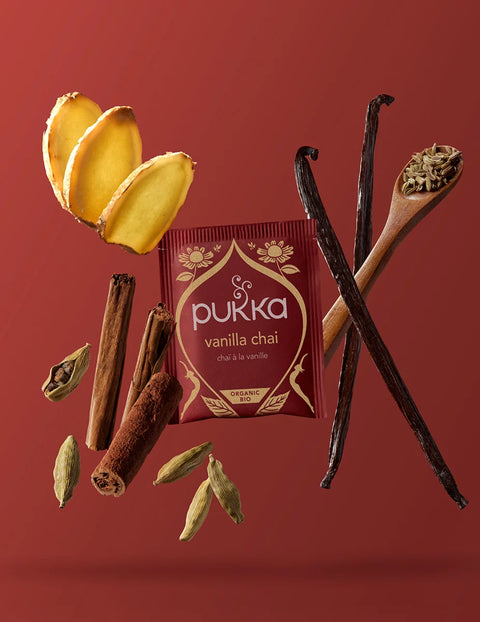 Pukka Vanilla Chai Teebeutel umgeben von Ingwer, Vanilleschoten, Zimt und Kardamom-Gewürzen.
