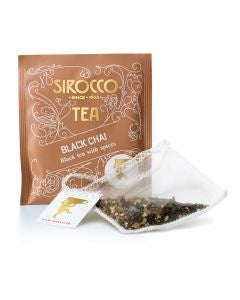 Ein bronzefarbenes Tee-Sachet für Sirocco „Black Chai“ (Schwarztee mit Gewürzen) neben einem transparenten Pyramidenteebeutel, der mit losem schwarzem Tee und sichtbaren Gewürzstücken gefüllt ist.