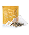 Ein goldgelbes Tee-Sachet für Sirocco „Ginger Lemon Dream“ Kräutertee, abgebildet mit einem transparenten Pyramidenteebeutel, der eine Mischung aus getrockneten Ingwerstücken und Zitronengras enthält.