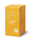 Eine goldgelbe Kartonverpackung für Sirocco „Ginger Lemon Dream“ Bio-Kräutertee mit weißen Ornamenten und einer Seitenwand, die die mehrsprachige Zutatenliste zeigt.