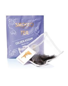 Ein lavendelfarbenes Tee-Sachet für Sirocco „Golden Assam“ Schwarztee, platziert hinter einem transparenten Pyramidenteebeutel, der mit feinen, dunklen Schwarzteeblättern gefüllt ist.