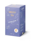 Eine lavendelfarbene Kartonverpackung für Sirocco „Golden Assam“ Bio-Schwarztee mit eleganten weißen Ornamenten und einer Seitenwand, auf der die mehrsprachige Zutatenliste steht.