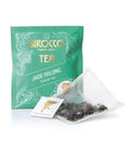 Ein türkisgrünes Tee-Sachet für Sirocco „Jade Oolong“ Grüntee neben einem transparenten Pyramidenteebeutel, der mit dunklen, teilfermentierten Oolong-Teeblättern gefüllt ist.