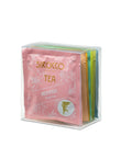 Transparente Geschenkbox mit einer Auswahl an bunten, einzeln verpackten Sirocco Teebeuteln, wobei die vorderste Packung "Red Kiss Fruit tea" ist.