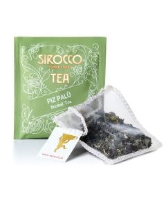 Ein olivgrünes Tee-Sachet für Sirocco „Piz Palü“ Kräutertee, abgebildet mit einem transparenten Pyramidenteebeutel, der eine Bergkräutermischung aus getrockneten grünen Blättern und Blüten enthält.
