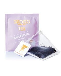 Ein zartviolettes Tee-Sachet für Sirocco „Purple Breeze“ Darjeeling-Tee hinter einem transparenten Pyramidenteebeutel, der mit dunklen, hochwertigen Schwarzteeblättern gefüllt ist.