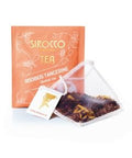 Ein orangefarbenes Tee-Sachet für Sirocco „Rooibos Tangerine“ Kräutertee neben einem transparenten Pyramidenteebeutel, der mit losem Rooibostee und Zitusschalen gefüllt ist.