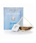 Ein hellblaues Tee-Sachet für Sirocco „Wellness Tea Balance“ neben einem transparenten Pyramidenteebeutel, der mit einer feinen Kräuterteemischung aus Fenchel und anderen Pflanzen gefüllt ist.