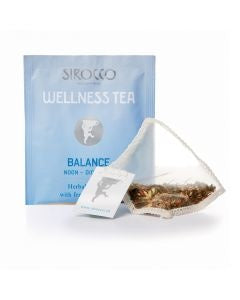 Ein hellblaues Tee-Sachet für Sirocco „Wellness Tea Balance“ neben einem transparenten Pyramidenteebeutel, der mit einer feinen Kräuterteemischung aus Fenchel und anderen Pflanzen gefüllt ist.