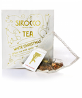 Ein weißes Tee-Sachet für Sirocco „White Christmas“ Tee mit goldenen festlichen Sternmustern und einem transparenten Pyramidenteebeutel, gefüllt mit weißem Tee, Apfelstücken und Gewürzen.