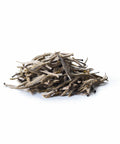 Ein kleiner Haufen loser Sirocco „White Silver Needle“ Weißtee mit Jasmin auf weißem Hintergrund, bestehend aus langen, schlanken und flaumigen, silberweißen Teeknospen.